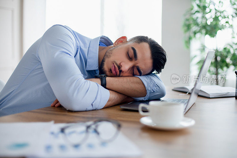 疲惫的阿拉伯商人睡在他的书桌前的笔记本电脑，过度工作，感觉疲惫的现代办公室