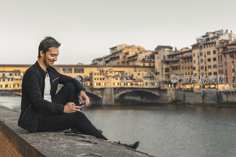 意大利佛罗伦萨托斯卡纳的一名年轻男子，面带微笑地看着智能手机，分享内容