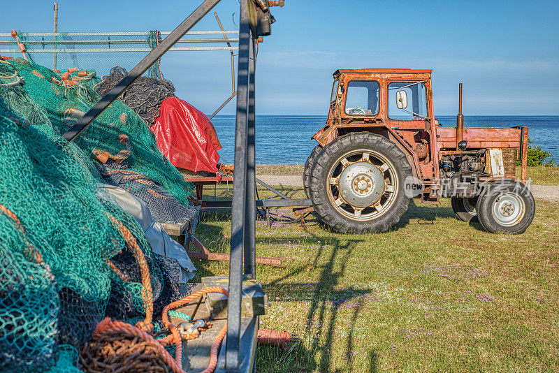 停滞、沉闷的捕鱼业:瑞典奥斯特伦的Stenshuvud国家公园，一辆旧拖拉机和未使用的渔网在海边被拖网拖到海里