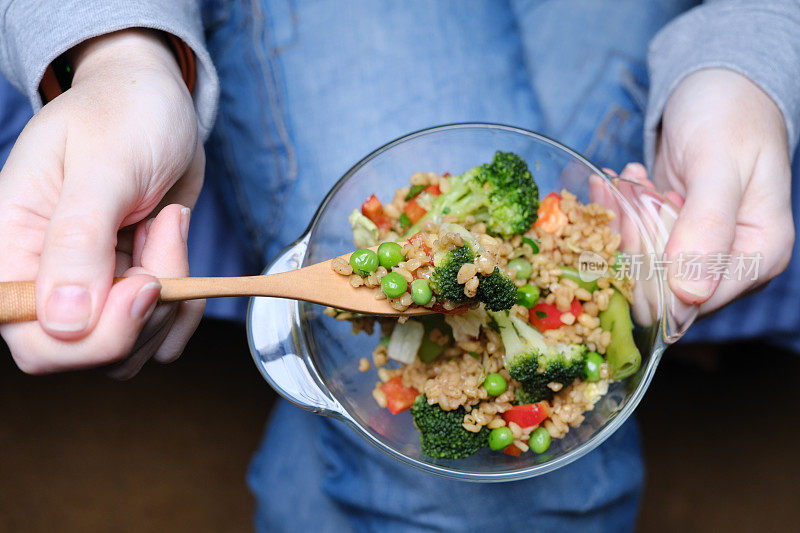 一个人把一碗碾碎的干小麦和蔬菜放在膝盖上