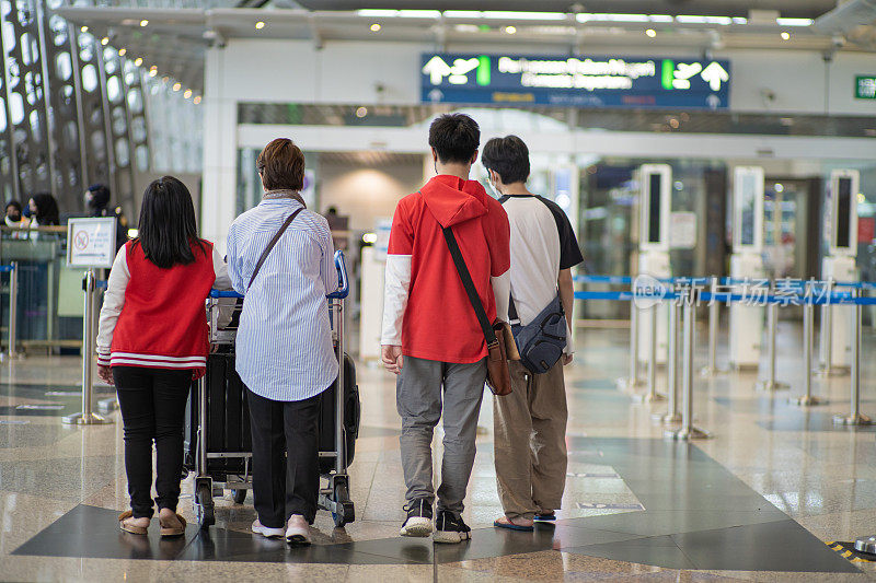 后视图亚洲华人家庭在机场登机口排队