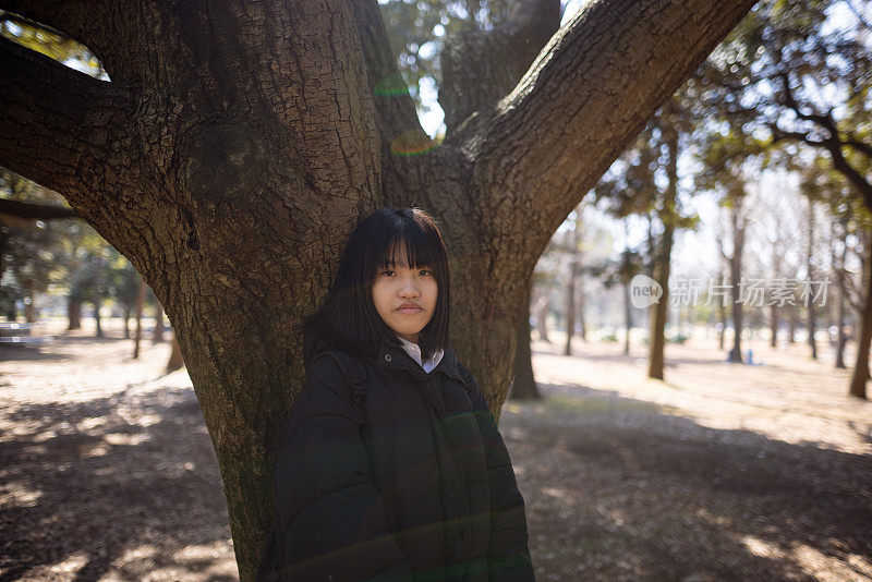 女学生的肖像倚在树在公园