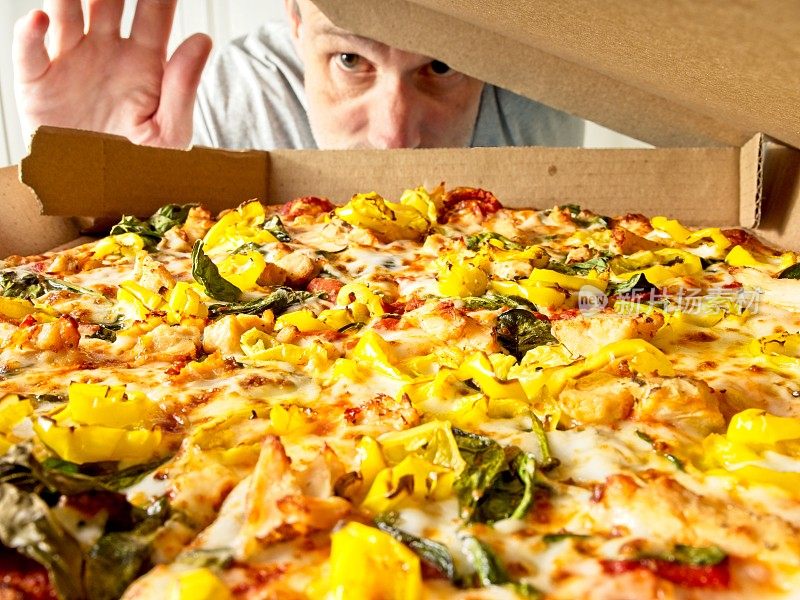 一家披萨店的盒子里新鲜的披萨打开了，一个男人的眼睛盯着美味的披萨