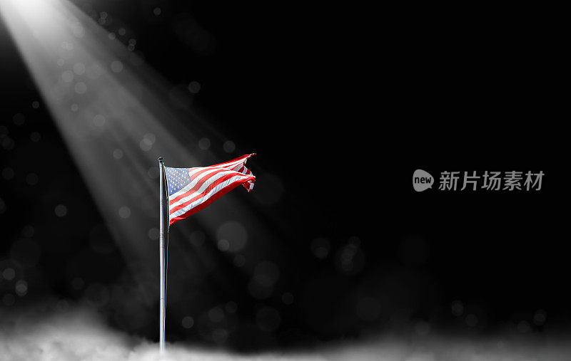 美国国旗在旗杆与光束在黑色的天空