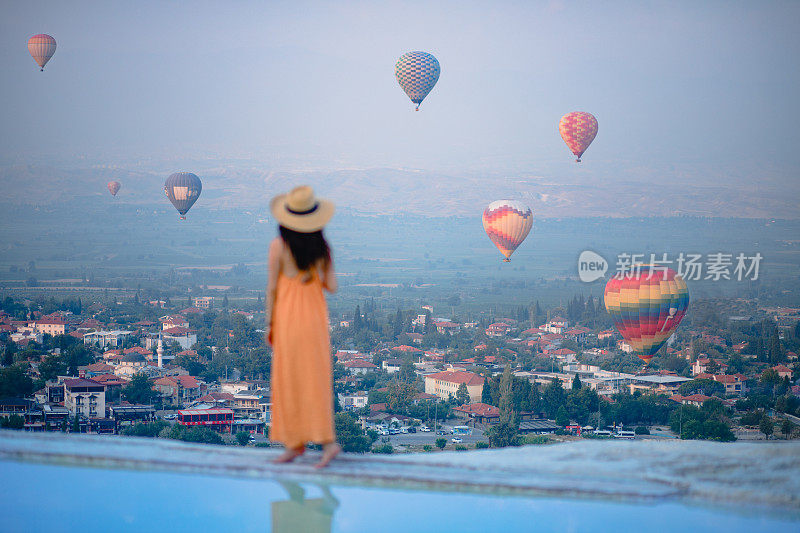 在土耳其德尼兹利的Pamukkale石灰华泳池里，美丽的游客女孩正在观看热气球