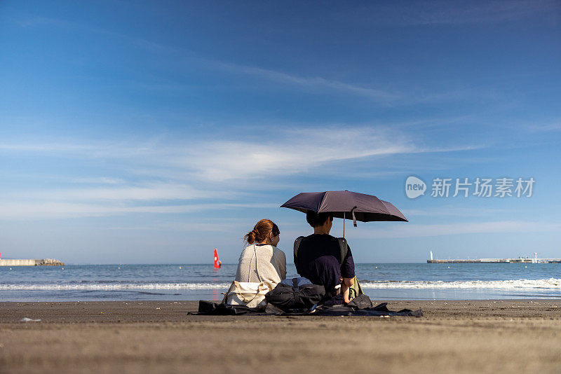 后视图一家人坐在海滩上，望着大海和天空