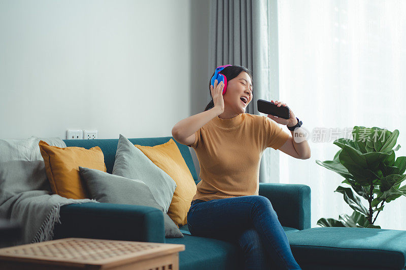 快乐的女人在家里用智能手机和耳机听音乐。