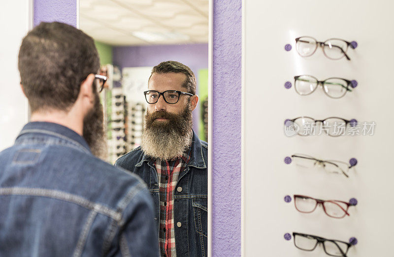 大胡子男子在眼镜店试眼镜。眼镜的选择