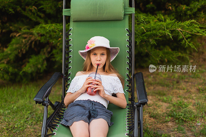 快乐的金发女孩穿着礼服，躺在后院的躺椅上。夏天的生活方式。的童年。