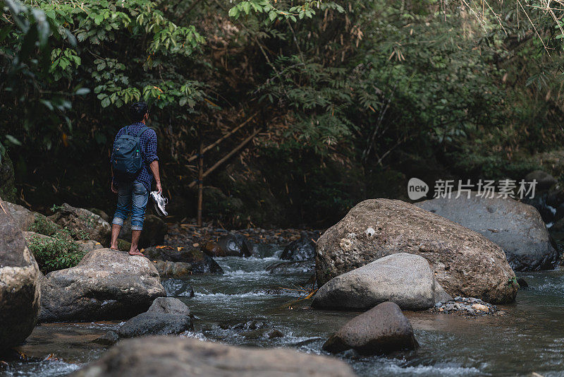 一名亚洲男子在热带雨林的小溪边穿着鞋子欣赏森林景色