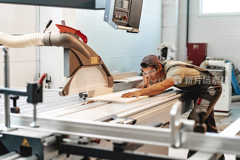 在家具厂，年轻的木匠正在用圆锯切割一块木头
