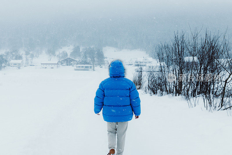 在大雪中漫步在斯堪的纳维亚村庄的蓝大衣女子欣赏冬天的童话