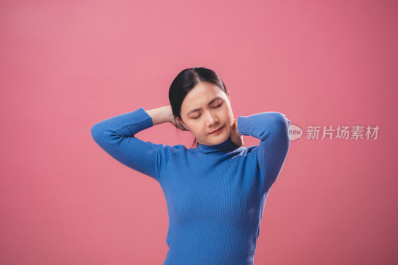 一名亚洲妇女颈部疼痛，孤立地站在粉红色的背景上。