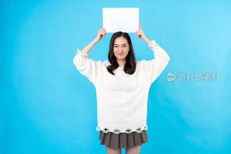 亚洲长发女模特站着，头上放一个白纸牌子，留出空间。用于插入文本或符号词。在蓝色背景的摄影棚里拍照