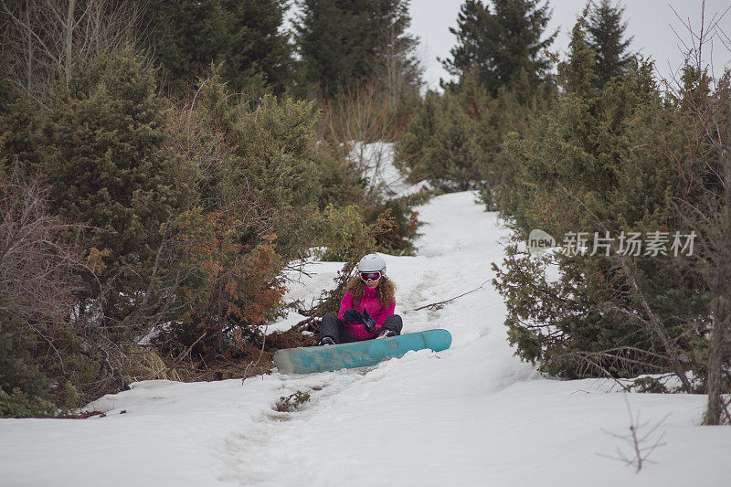 年轻女子在空中度假时坐在雪地上调整她的滑雪板