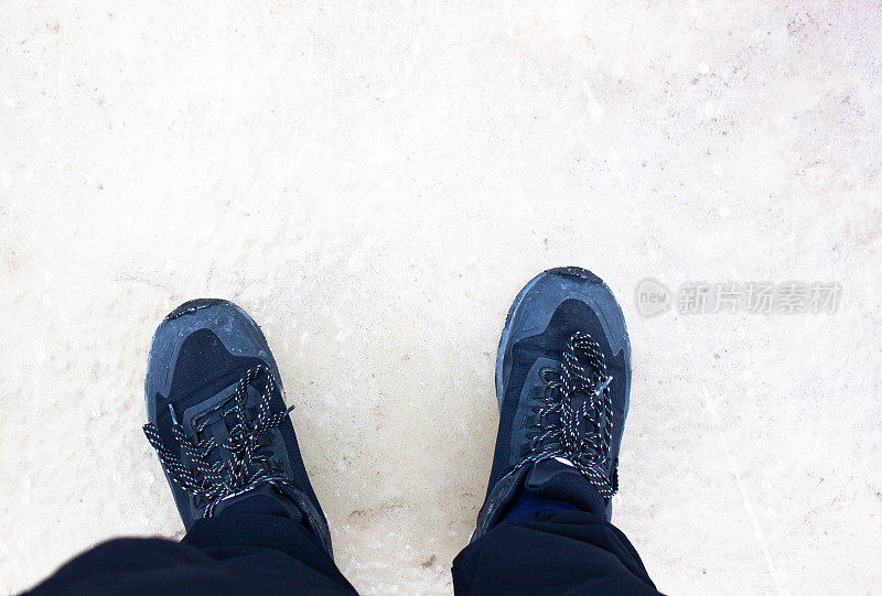 雪地里穿着运动鞋的脚。冬天穿着运动鞋的男子视角。