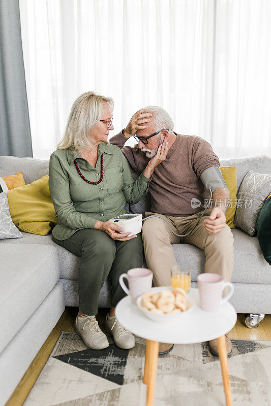 老夫妇在家测血压。妻子正在用血压计检查丈夫手臂上的血压