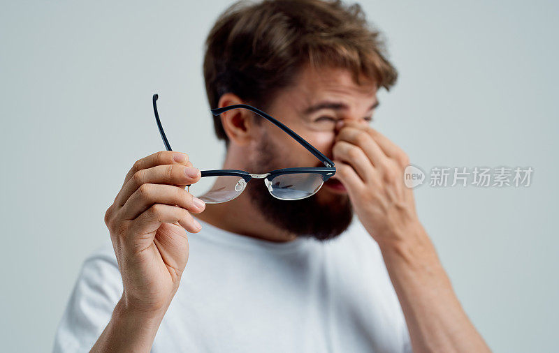 一个眯着眼睛的男人手里拿着眼镜，背景很浅，视力有问题