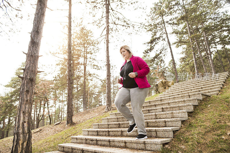 一个超重的女人在城市公园里跑步，从楼梯上跑下来。肥胖人群适合户外锻炼。