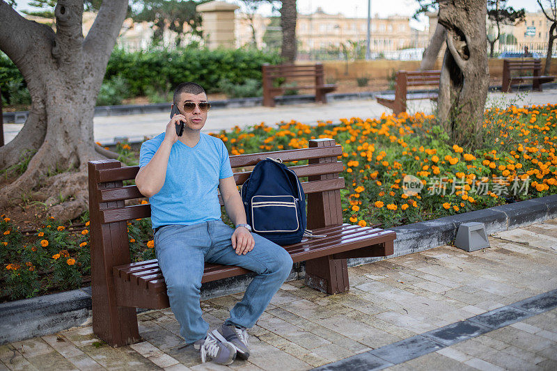 一个年轻人正坐在长凳上用他的手机。