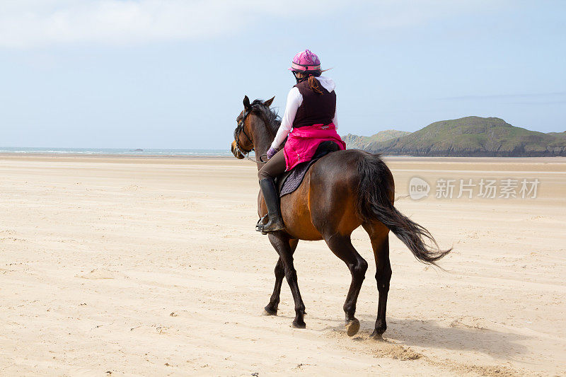 孤独的女骑手和她的海湾马喜欢在威尔士安格尔西岛的空旷海滩上骑马