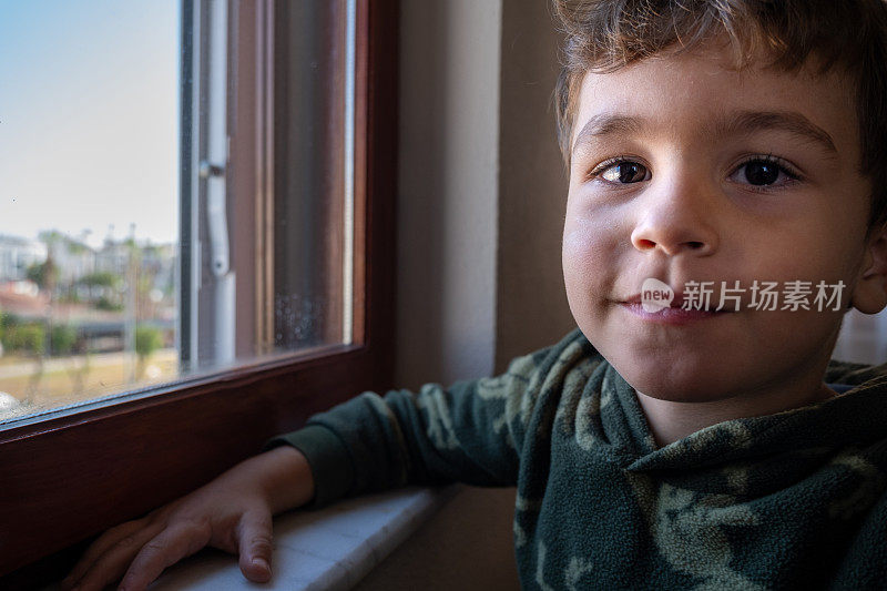 4一个四岁的男孩看着窗边的照相机