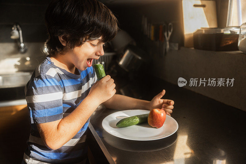 8岁的混血男孩在厨房里吃黄瓜