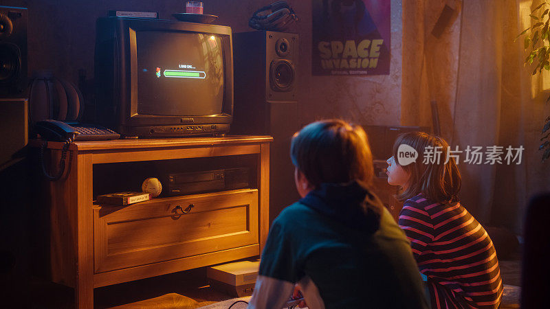 怀旧的童年概念:年轻的男孩和女孩在家里的复古电视机上玩老派街机视频游戏，房间内部的年代是正确的。等待关卡加载的孩子。