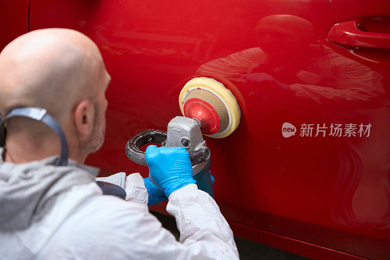 一名男子正在修理一辆红色汽车的车身