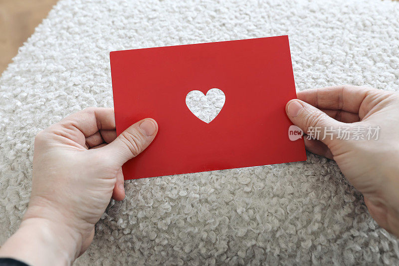 特写的妇女手拿红色的圣瓦伦丁节贺卡剪出心形。2月14日假期。仿羔皮呢背景。爱,激情。母亲节明信片。婚礼的邀请。