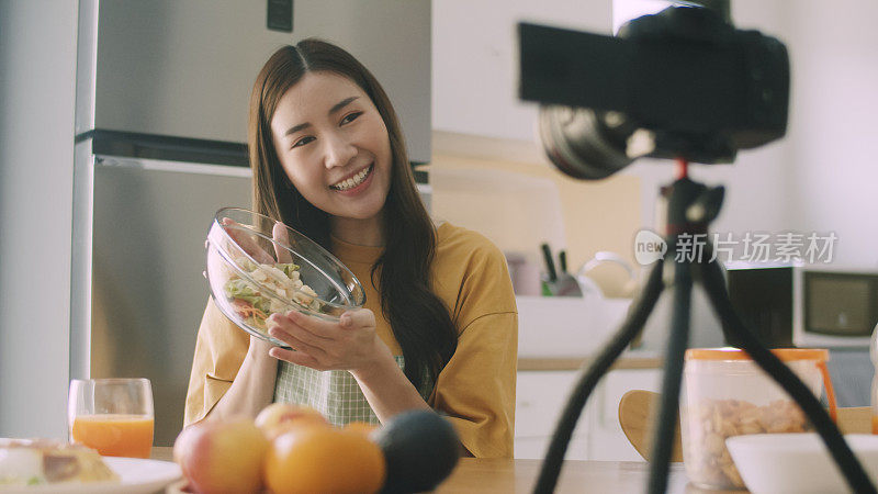 亚洲博主网红录制视频，一边在家厨房做饭，一边制作沙拉水果和蔬菜。社交媒体影响者概念。