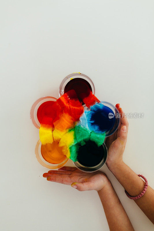 孩子用手拿着彩虹食物的颜色用纸和水做实验。茎的话题