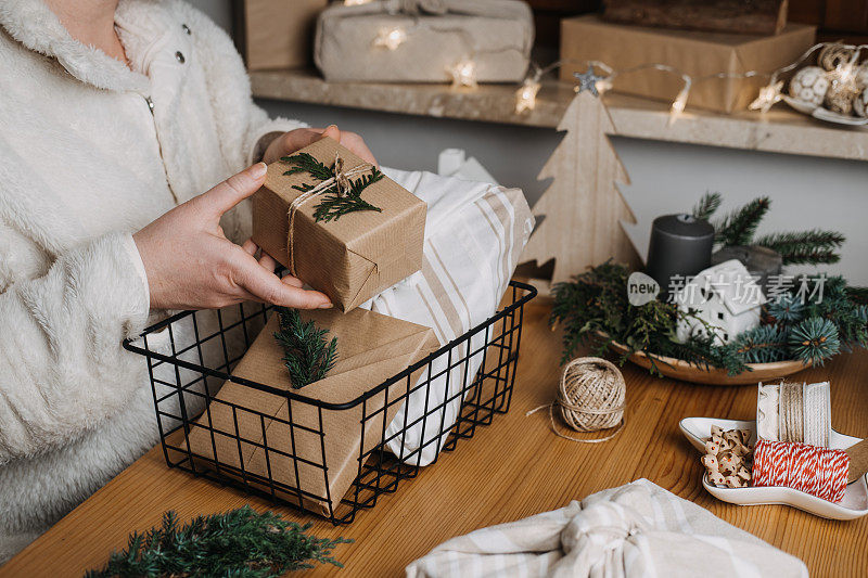 圣诞节零浪费环保再利用包装礼品过程。零浪费可重复使用的工艺纸可持续的礼物用工艺纸与绿叶在家里的桌子上
