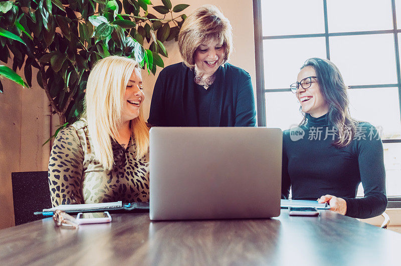 工作中的女性，会议桌旁拿着笔记本电脑的三位女企业家，商业伙伴、同事或客户和代理商