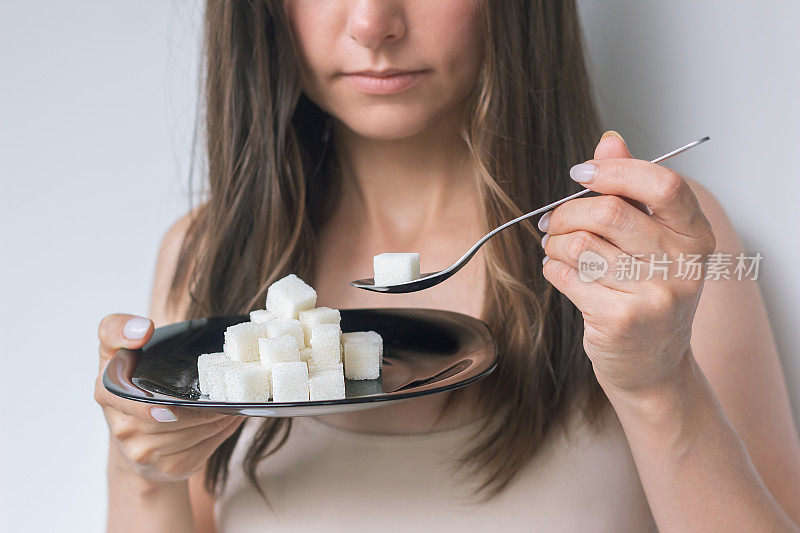 年轻女子面前拿着一个装着精制糖的黑色盘子，另一只手拿着一个装着糖的勺子，想要吃