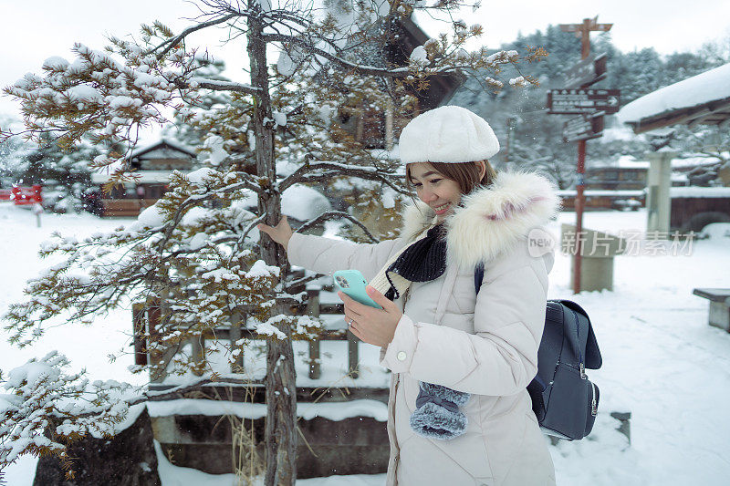 美丽的女游客用电话享受她的日本之旅在雪的冬天