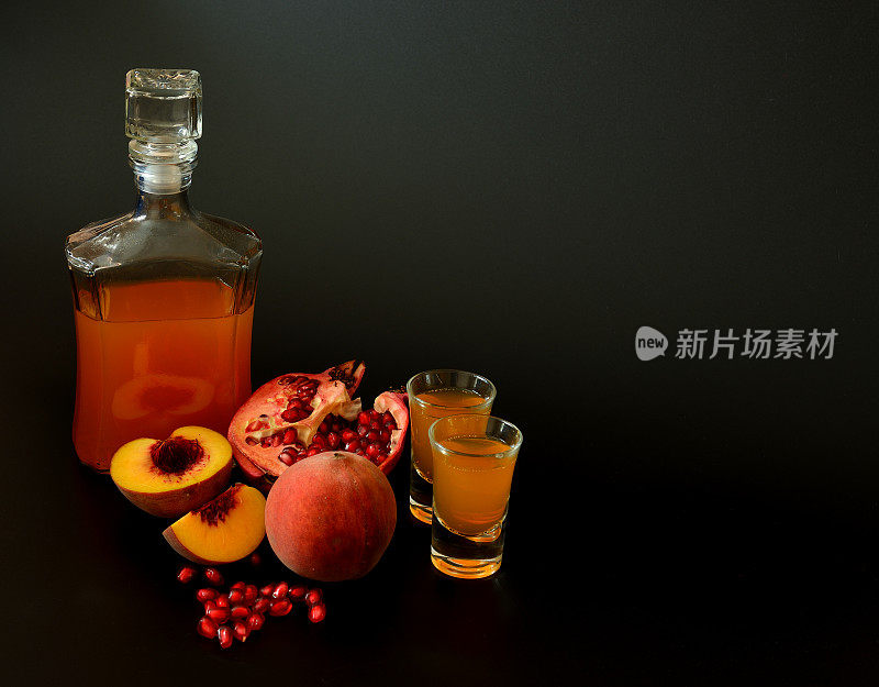 一瓶和两杯自制的水果利口酒，背景是黑色的，旁边是熟桃子和碎石榴。