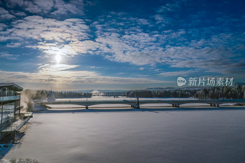 瑞典北部Lycksele结冰的乌姆河上的桥梁风景。冰封的河面上覆盖着刚下过的雪，冬日的阳光洒在蓝天上。