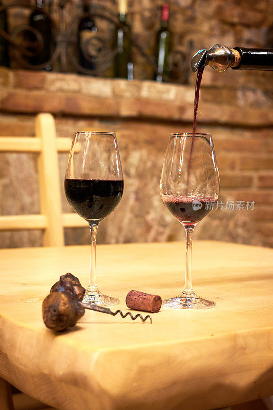 侍酒师将红酒倒入长柄酒杯。古老的红砖酒窖里木桌上的酒杯
