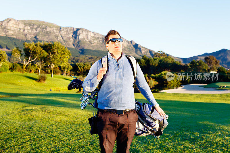 微笑的年轻高尔夫球手大步走过球场，提着他的包
