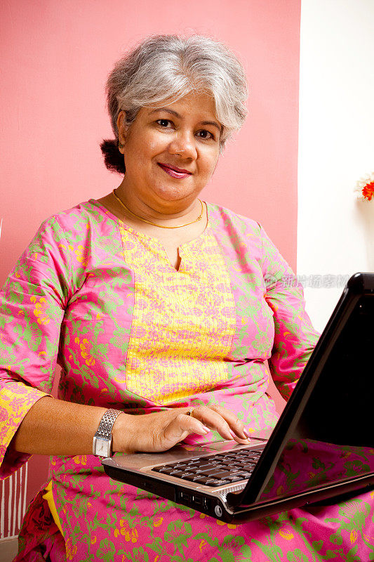 愉快的印度迷人的成年女人在笔记本电脑上工作