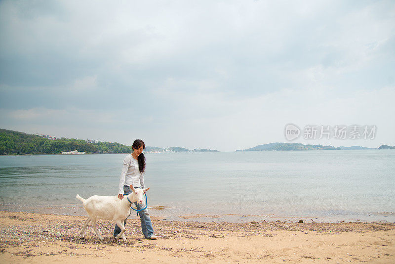 一个女人和她的宠物山羊在海滩上散步