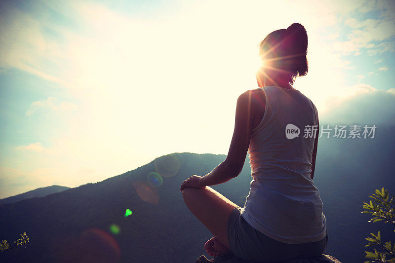 年轻的瑜伽女子在日出的山顶