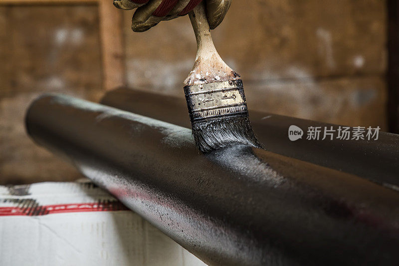 用刷子把旧铁管刷成黑色。男人是肮脏的工作。
