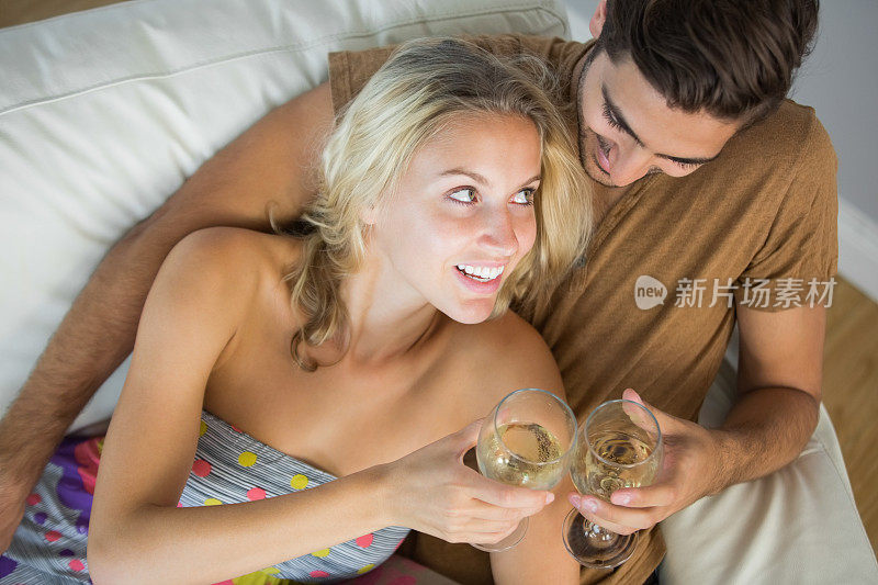 一对可爱的年轻夫妇躺在沙发上喝着白葡萄酒
