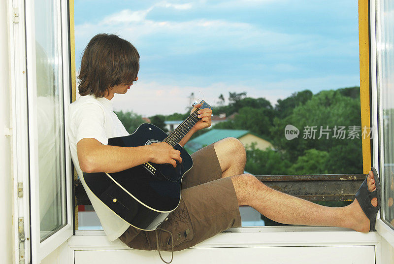 一个年轻人坐在窗户上弹吉他