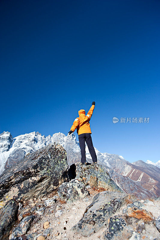 一位女性登山者举起一只手，背景是喜马拉雅山