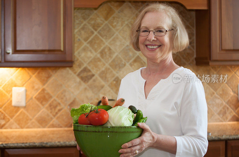 年长的女人在厨房里端着一碗新鲜的蔬菜