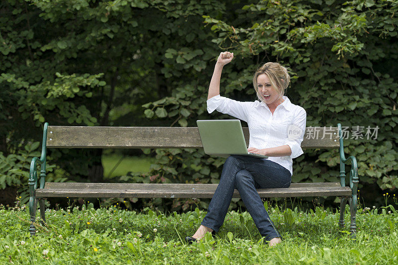 一个在公园长椅上拿着笔记本电脑的快乐年轻女人