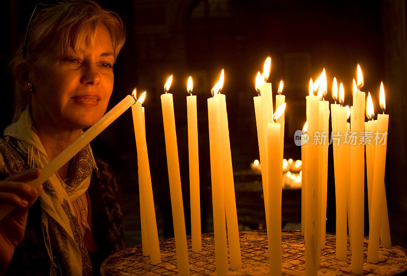 女人在教堂点燃祈祷蜡烛;黑色背景